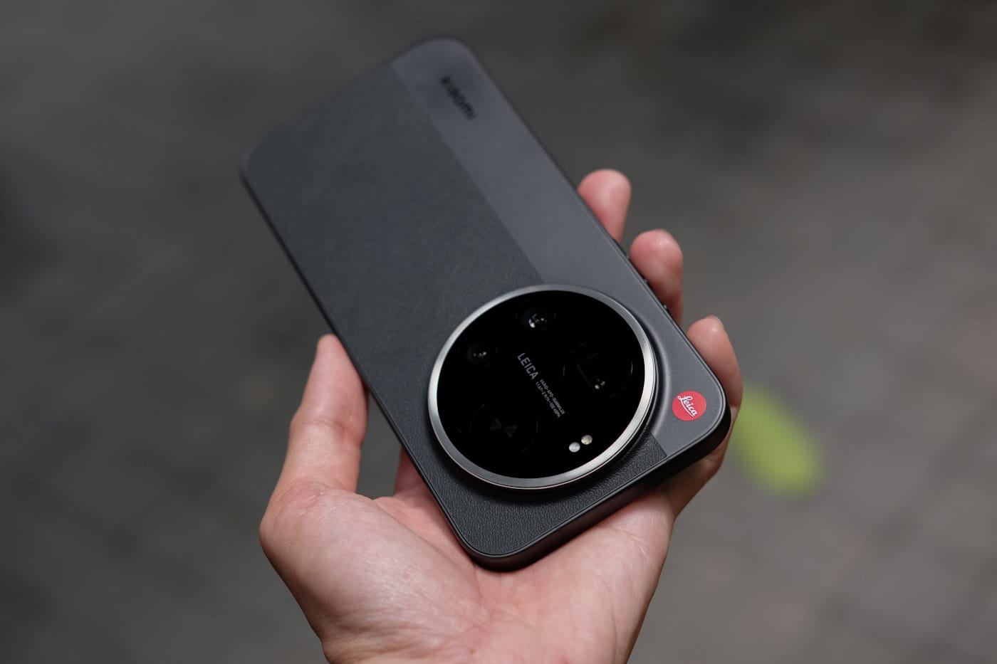 Hand holding a dark smartphone with a large leica camera