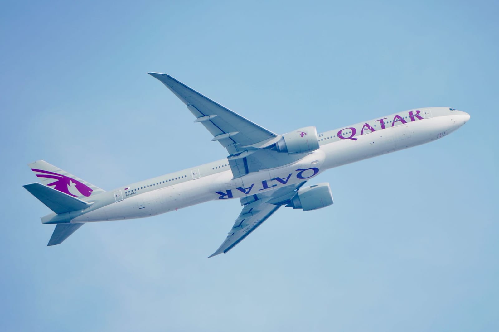 High-angle view of a Qatar Airways Boeing 777 airplane soaring in a clear blue sky, showcasing aviation elegance.